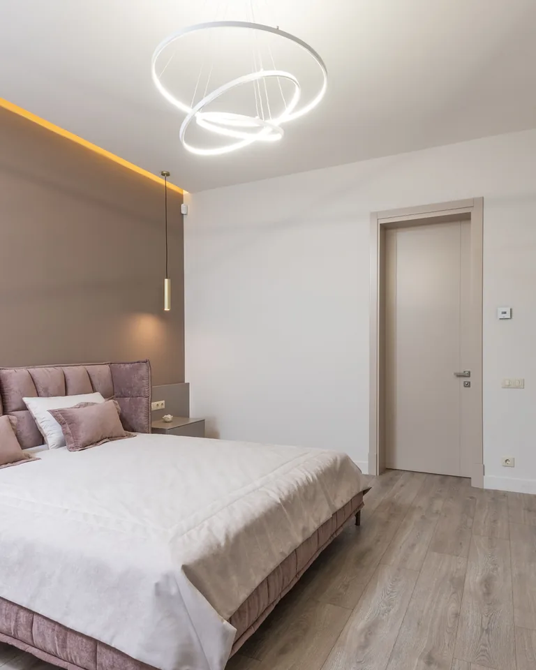 Bedroom with light wood walls, pink upholstered bed and modern chandelier