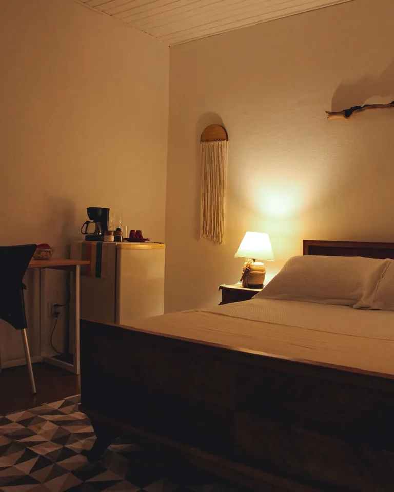 Warm wall-mounted reading light glowing beside the bed in a small bedroom