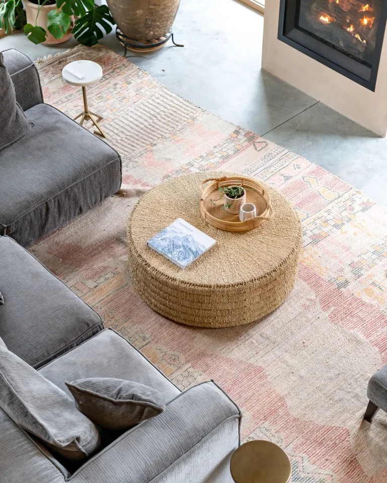 Overhead view of a patterned rug anchoring a gray sofa and round jute coffee table