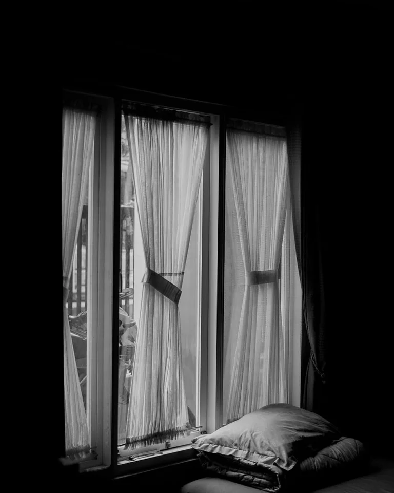 White curtains hanging on a black curtain rod in a bedroom